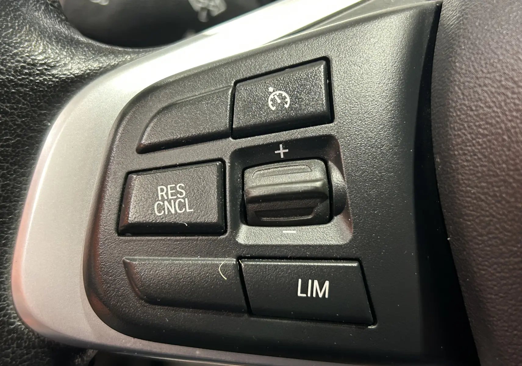 Gros plan sur les boutons de régulateur de vitesse au volant côté gauche d'une BMW X1 blanche de 2018.
