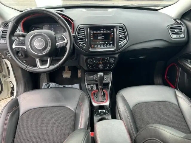 Vue intérieure avant du Jeep Compass 1.3 blanc de 2020, avec volant multifonction et finitions rouges autour du levier de vitesses.
