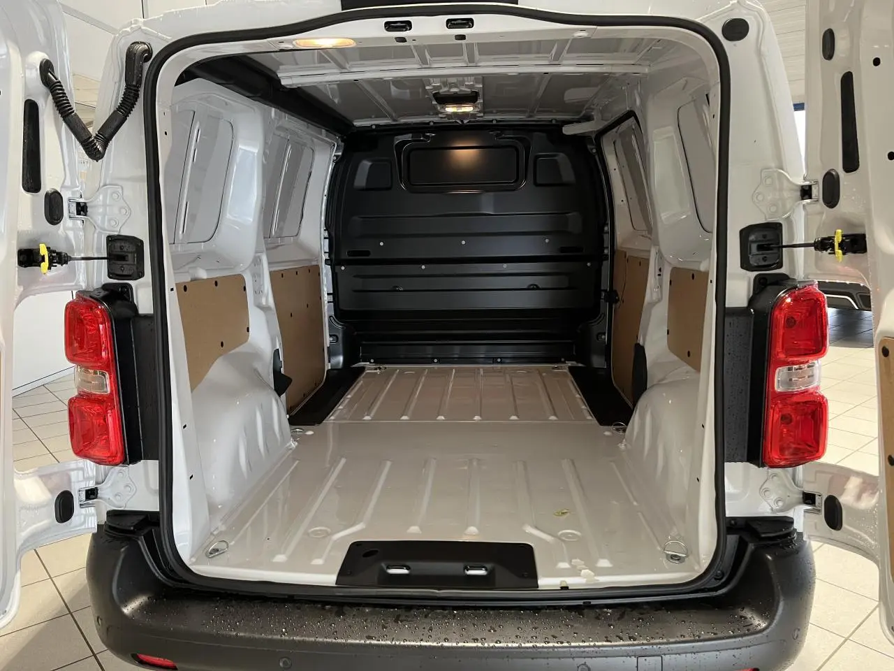 Vue arrière du Peugeot Expert Fourgon blanc 2024, portes ouvertes dévoilant l'espace de chargement vide et ses panneaux latéraux clairs.