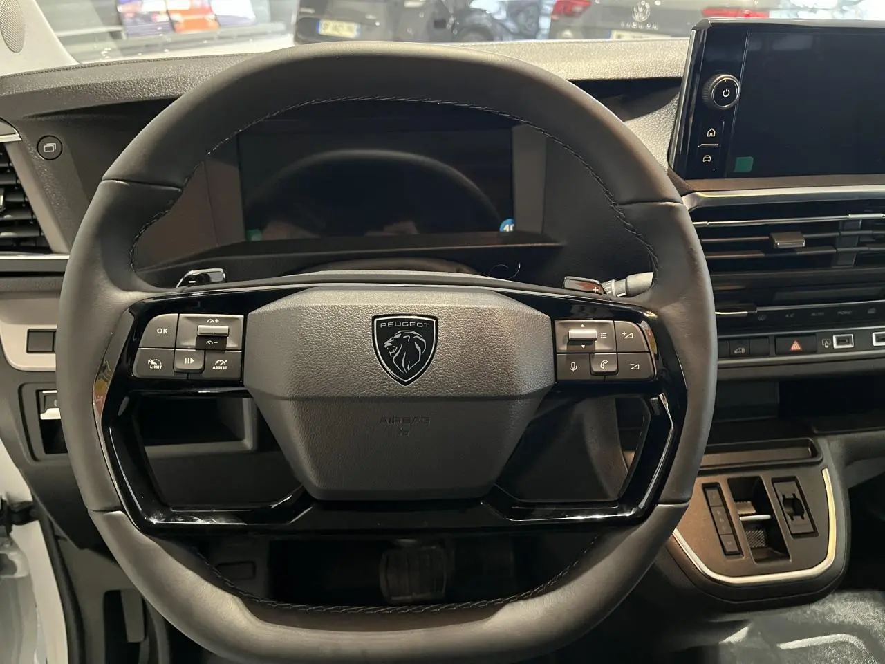 Vue rapprochée du volant en cuir noir du Peugeot Expert Fourgon 2024 avec commandes intégrées et tableau de bord moderne.