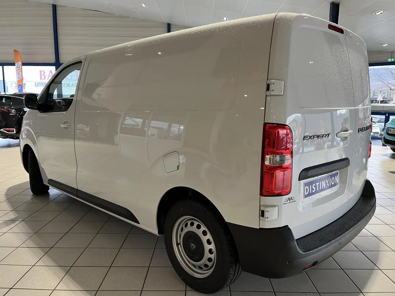 Vue 3/4 arrière droite d'un Peugeot Expert Fourgon blanc 2024 en showroom avec logo et feux arrière visibles.