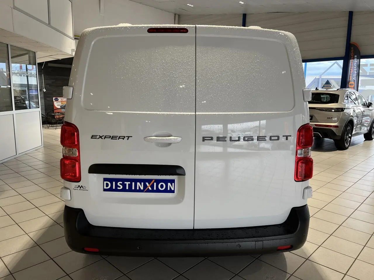 Vue arrière d'un Peugeot Expert Fourgon blanc 2024 avec feux rouges verticaux et logo distinctif sur portes battantes.