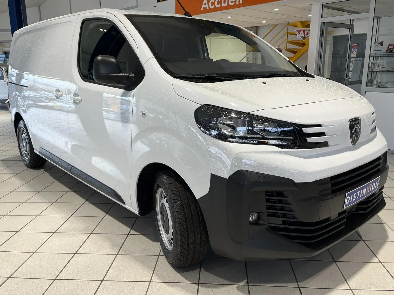 Peugeot Expert Fourgon blanc vu en 3/4 avant droit, avec calandre noire et projecteurs modernes en intérieur showroom.