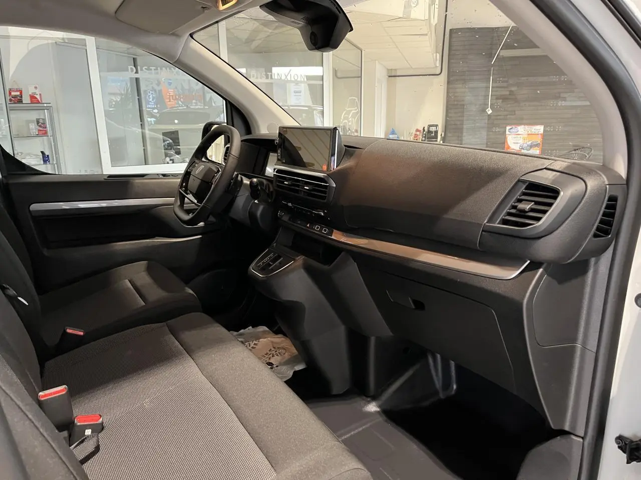 Intérieur côté conducteur du Peugeot Expert Fourgon blanc 2024, planche de bord noire avec écran tactile et sièges tissu bi-ton noir-gris.