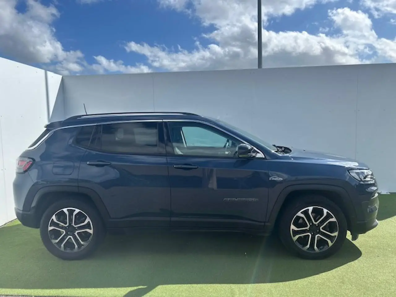 Jeep Compass 2022 bleu métallisé en profil côté gauche, avec jantes alliage et barres de toit visibles.
