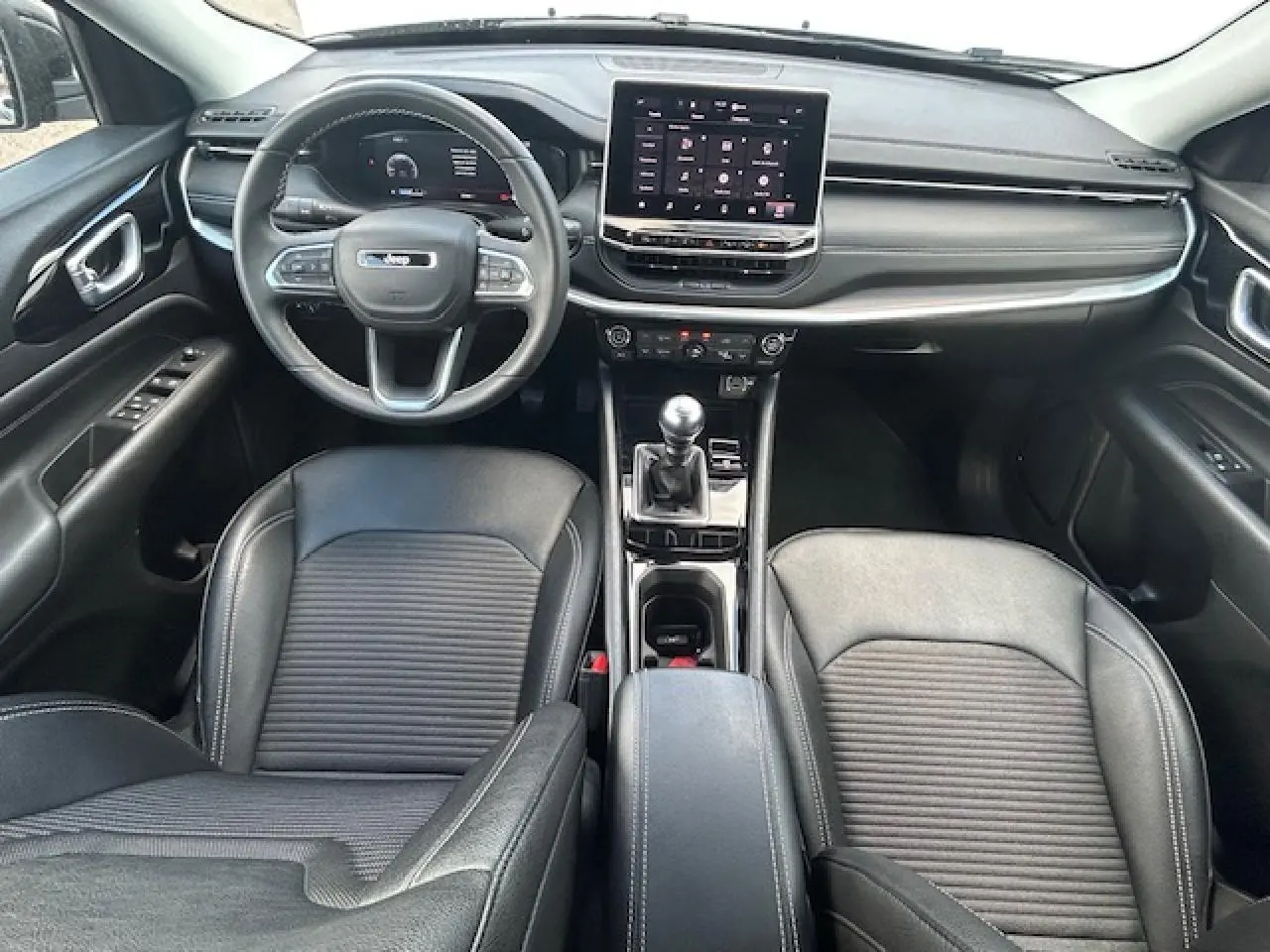Vue intérieure avant du Jeep Compass 2022 avec tableau de bord noir, écran tactile et levier de vitesses manuel.