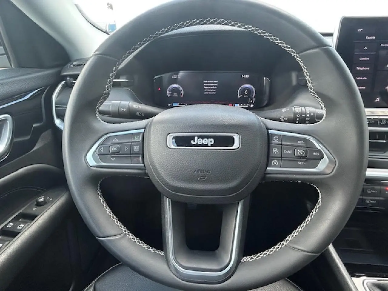 Vue rapprochée du volant noir avec surpiqûres blanches et tableau de bord numérique du Jeep Compass 2022.