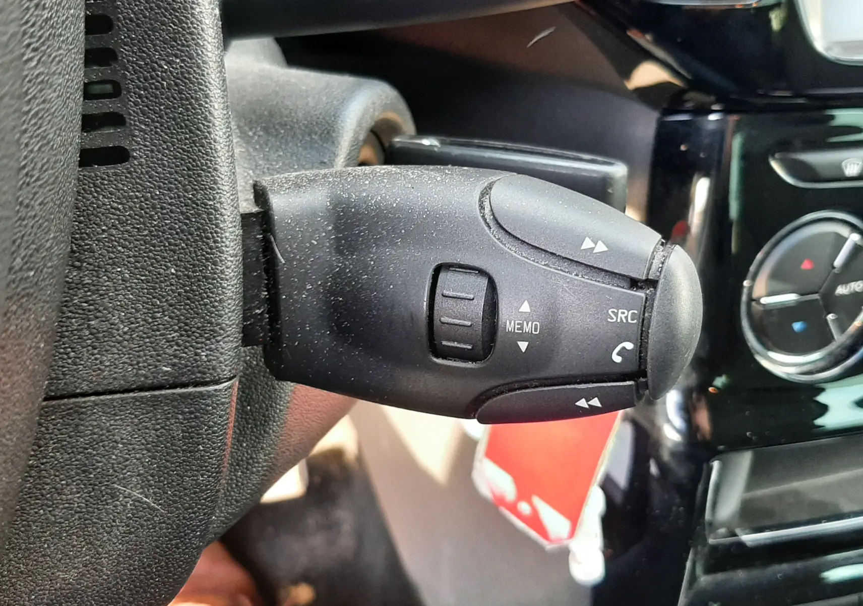 Gros plan sur la commande au volant côté gauche d'une Citroën C3 noire, avec tableau de bord et climatisation en arrière-plan.