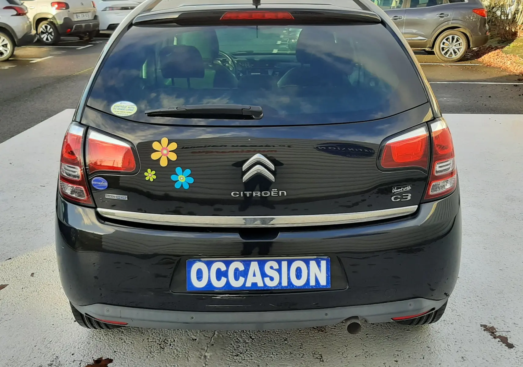 Vue arrière d'une Citroën C3 noire de 2016 avec stickers fleurs colorées et plaque "OCCASION" visible.