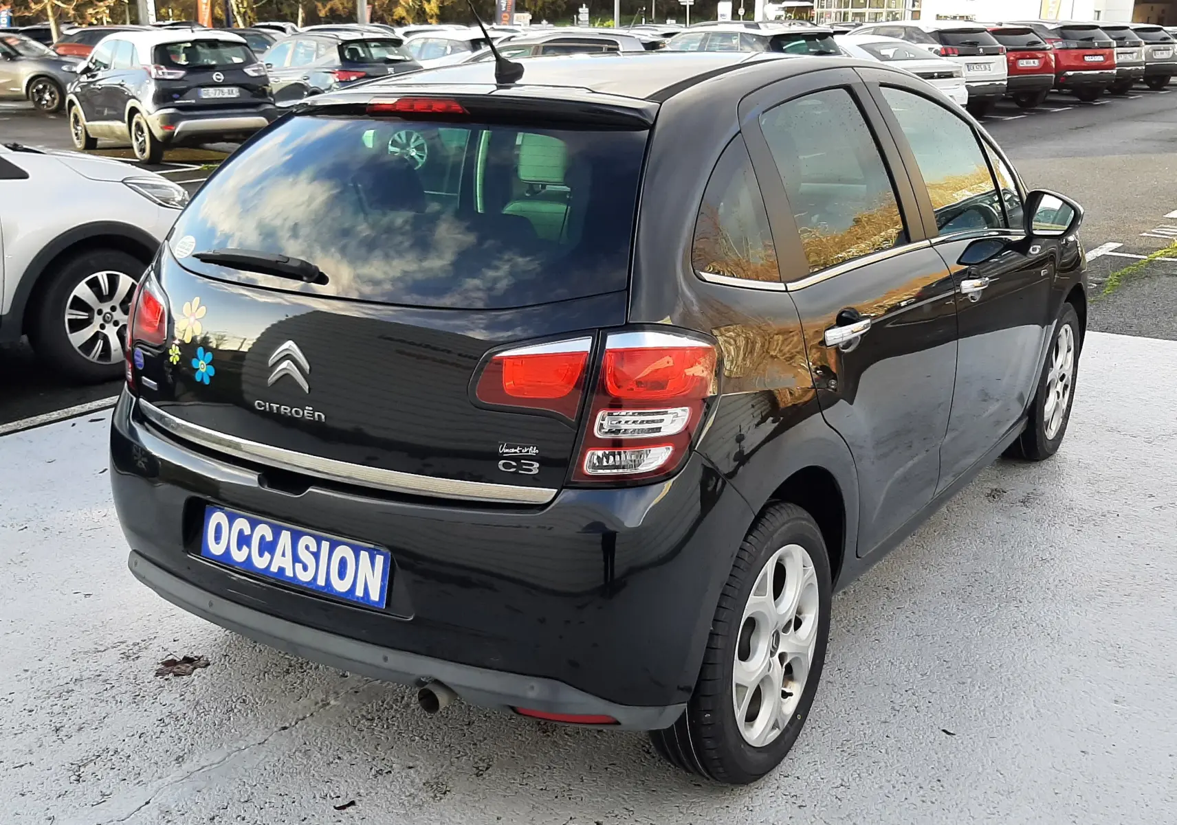 Vue 3/4 arrière droite d'une Citroën C3 noire de 2016 avec décorations florales colorées sur le coffre.