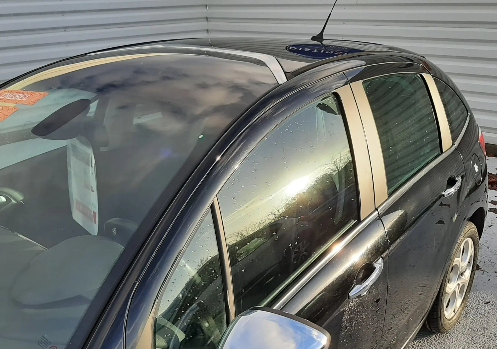 Vue 3/4 avant droit d'une Citroën C3 noire 2016 avec rétroviseur chromé et toit panoramique visible.