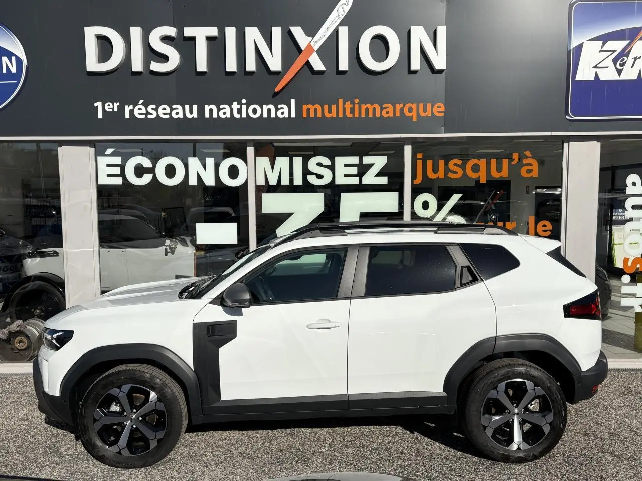 Profil droit du Dacia Duster 1.6 Hybrid blanc métallisé avec jantes alliage noires et barres de toit noires.