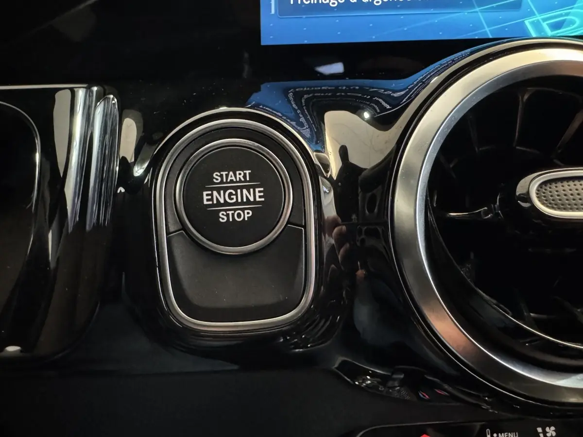 Gros plan sur le bouton start/stop moteur noir entouré de chrome dans l’habitacle du Mercedes GLA 250 e gris foncé.
