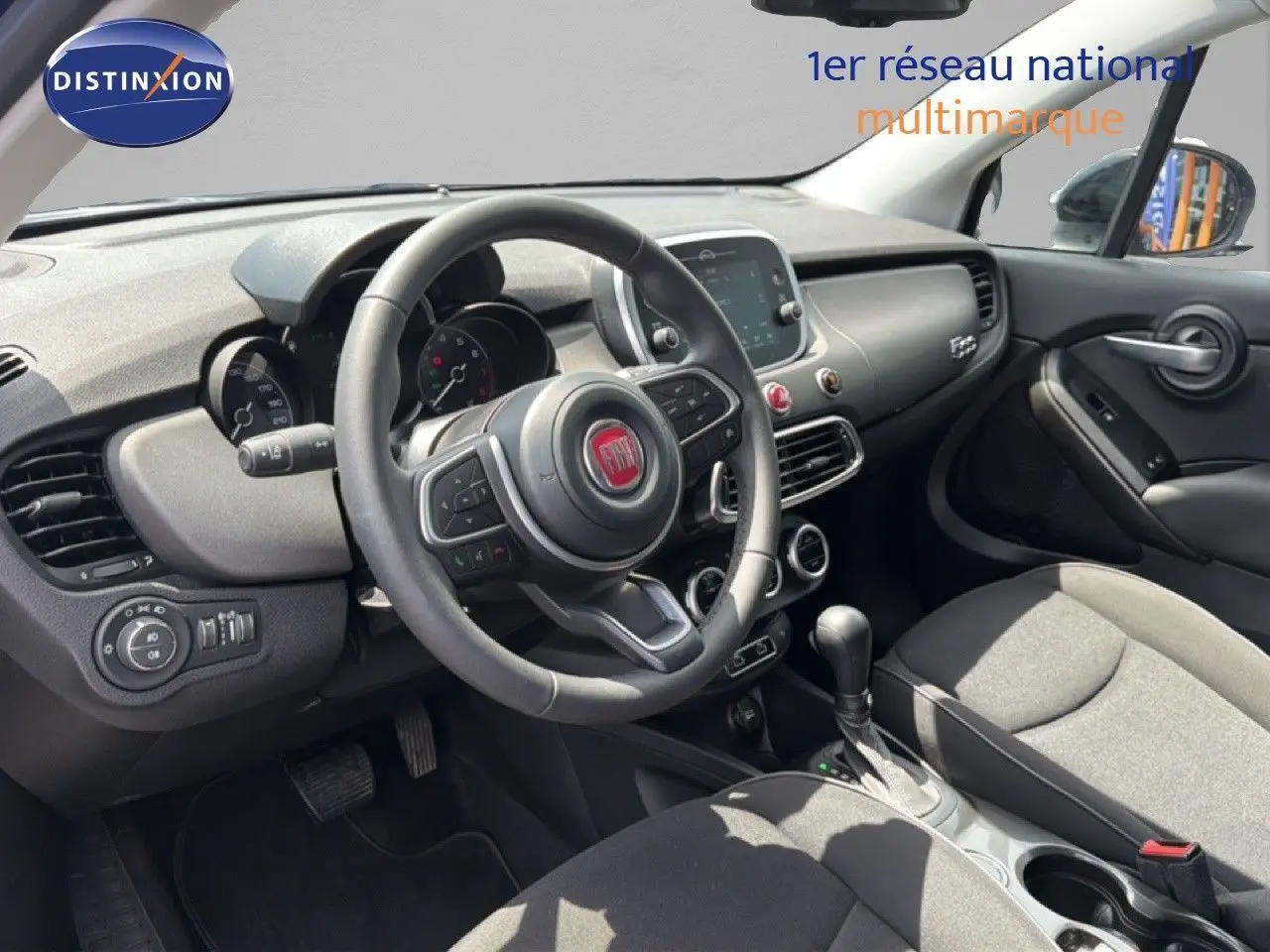 Vue intérieure côté conducteur du tableau de bord et volant de la FIAT 500X 2024, finition noire avec écran tactile central.