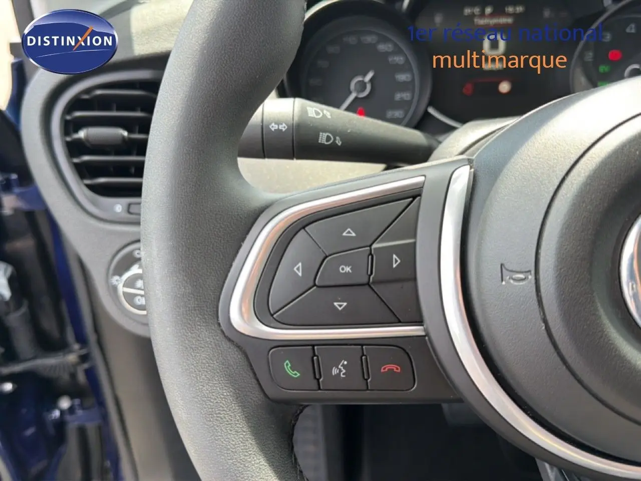 Gros plan sur le volant de la FIAT 500X bleu Venezia, montrant les commandes intégrées et la partie gauche du tableau de bord.