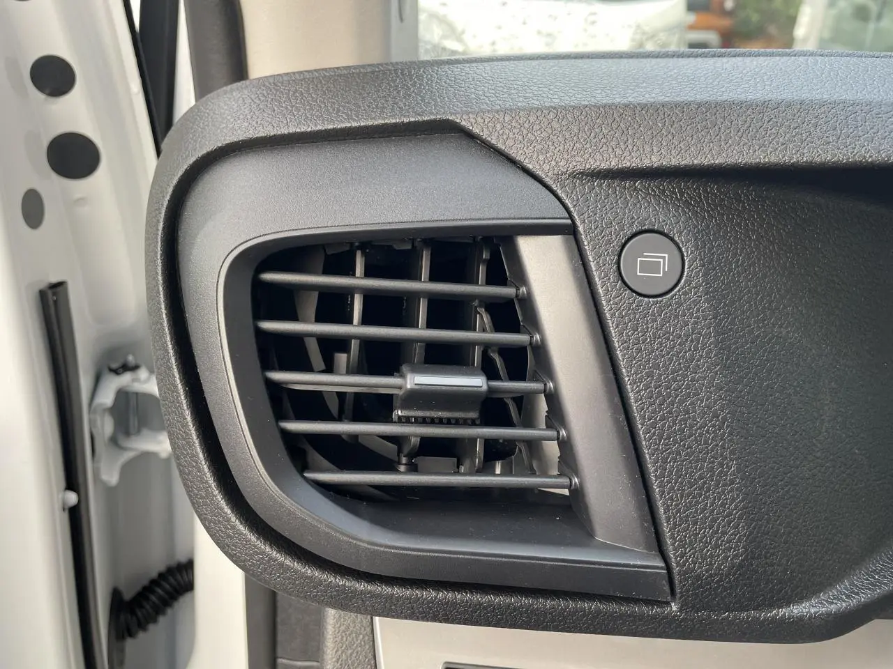 Détail de la grille d'aération noire sur le tableau de bord côté conducteur d'un Opel Vivaro blanc 2024.