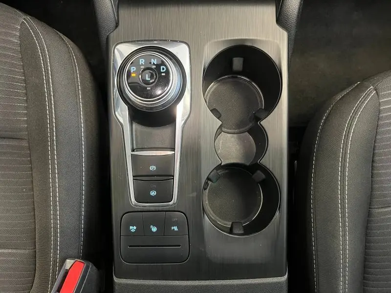 Vue plongeante sur la console centrale noire du Ford Kuga 2022 avec sélecteur rotatif de boîte auto et porte-gobelets.