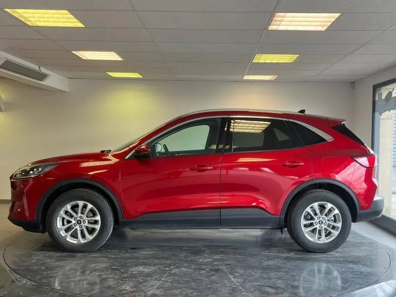 Profil droit d'un Ford Kuga 2022 hybride en rouge Premium Lucid avec toit panoramique dans un showroom.