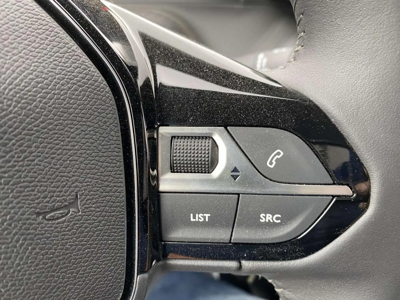 Gros plan sur les commandes du volant noir métallisé d'une Peugeot 208 2023, boutons list, SRC et appel téléphonique.