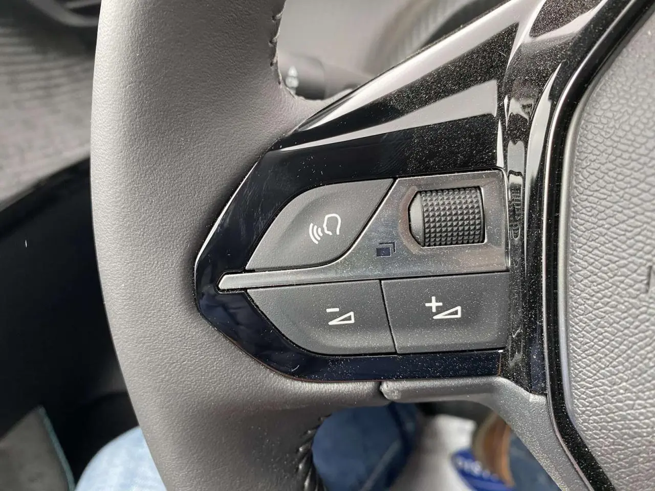 Gros plan sur les commandes audio et vocales au volant d'une Peugeot 208 noire métallisée de 2023.