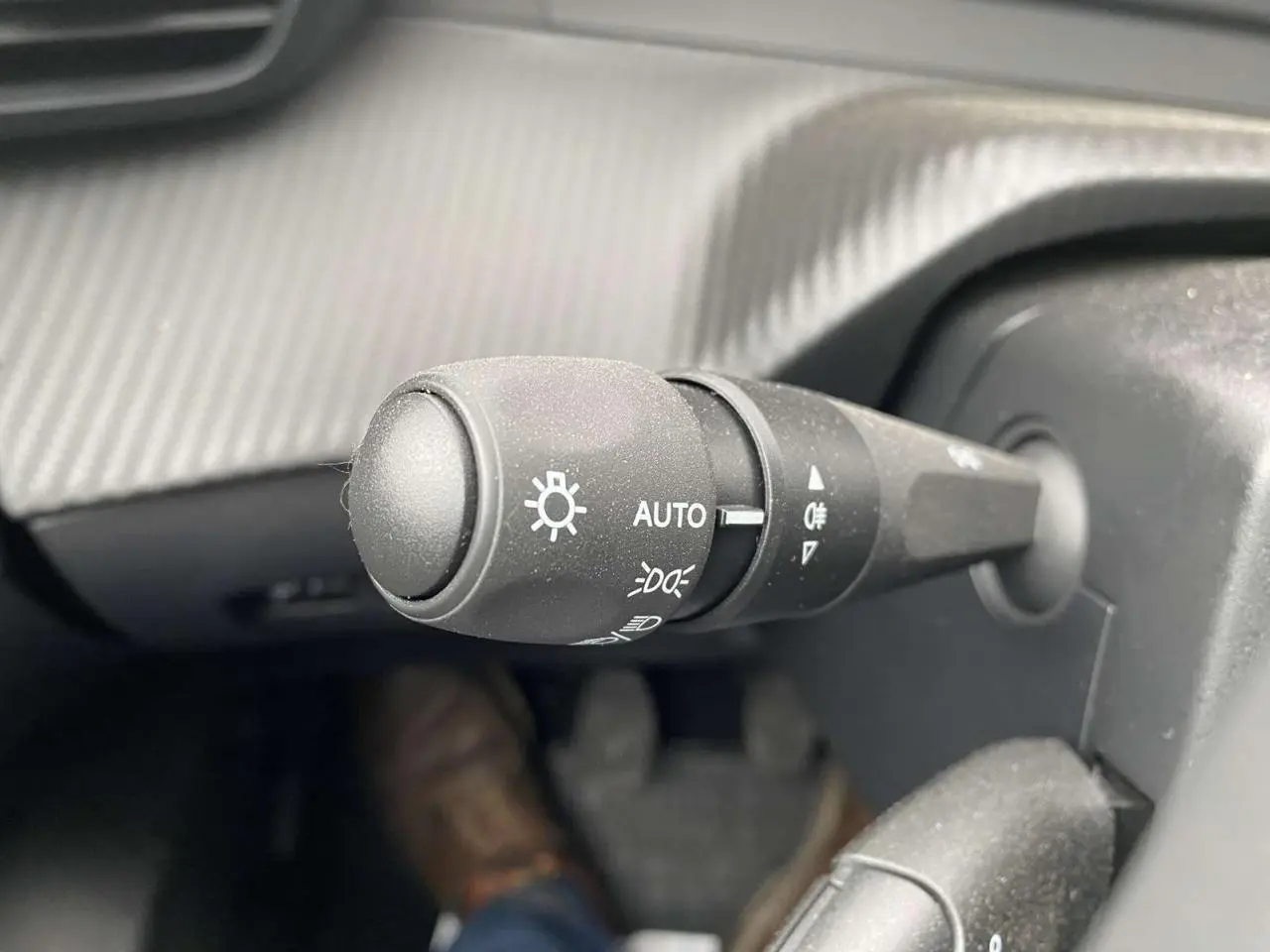 Gros plan sur la commande des feux avec réglage automatique dans l'habitacle d'une Peugeot 208 noire métallisée 2023.