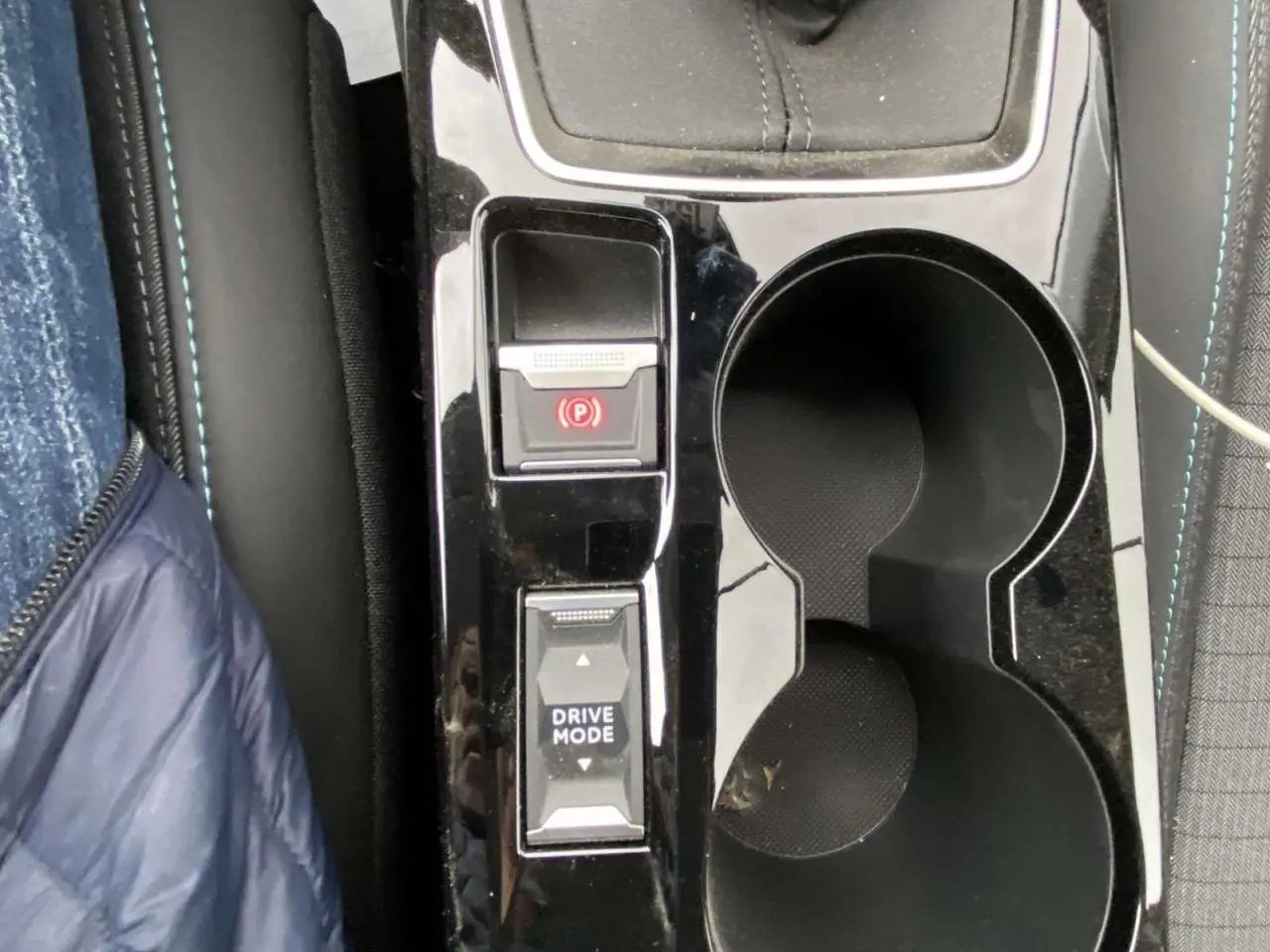 Gros plan sur la console centrale noire brillante d’une Peugeot 208 2023 avec frein à main électrique et bouton Drive Mode.