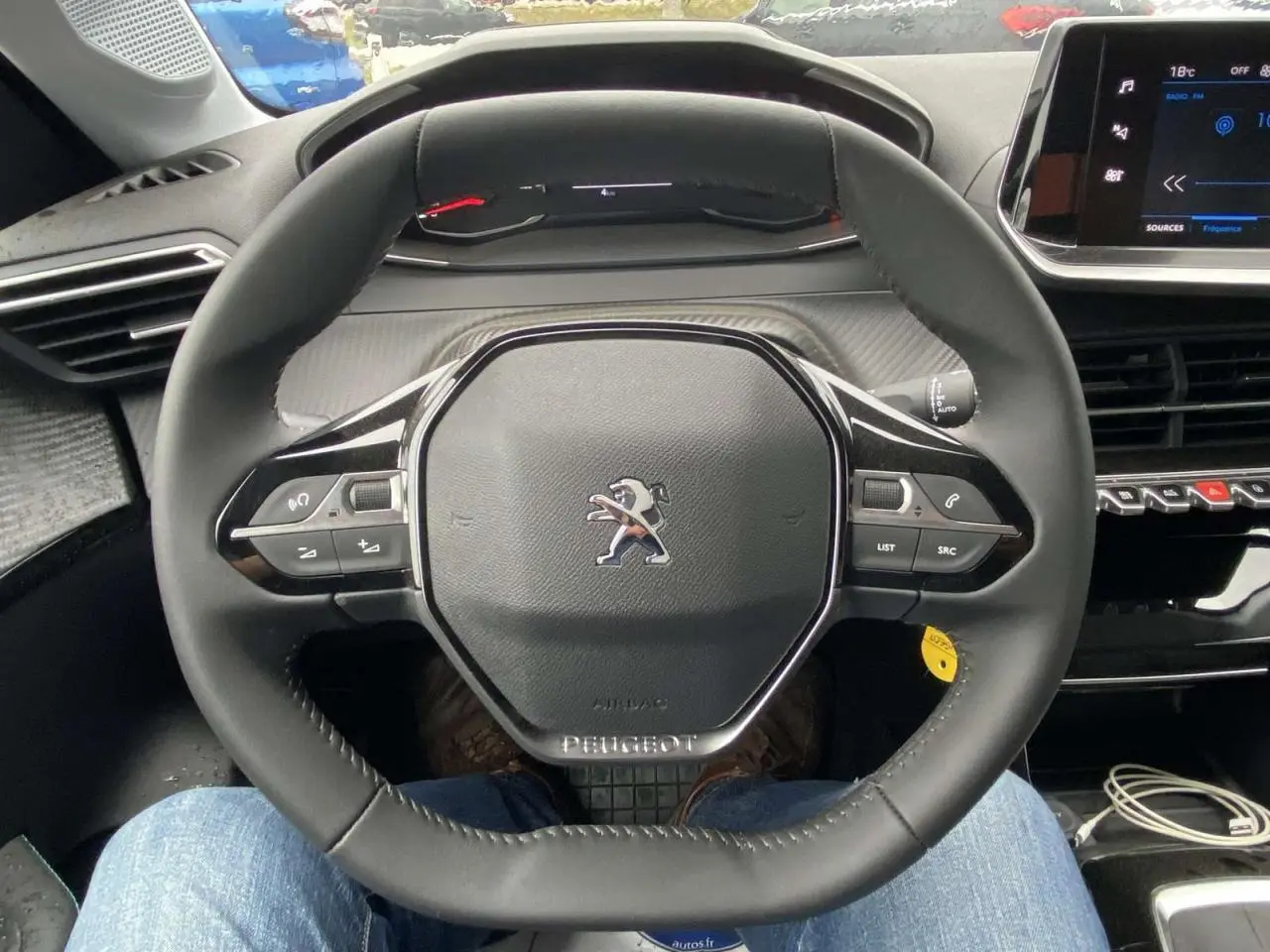 Vue intérieure centrée sur le volant cuir du Peugeot 208 2023 avec tableau de bord numérique et écran tactile.