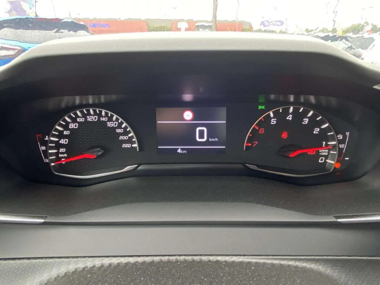 Vue rapprochée du tableau de bord numérique de la Peugeot 208 noire, affichant 0 km/h et 4 km au compteur.