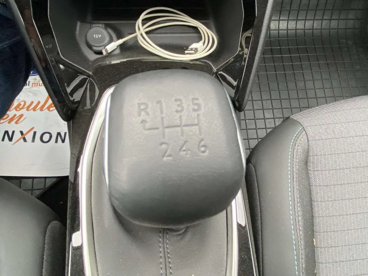 Gros plan sur le levier de vitesse manuel de la Peugeot 208 2023, intérieur noir avec surpiqûres bleues et câble USB.