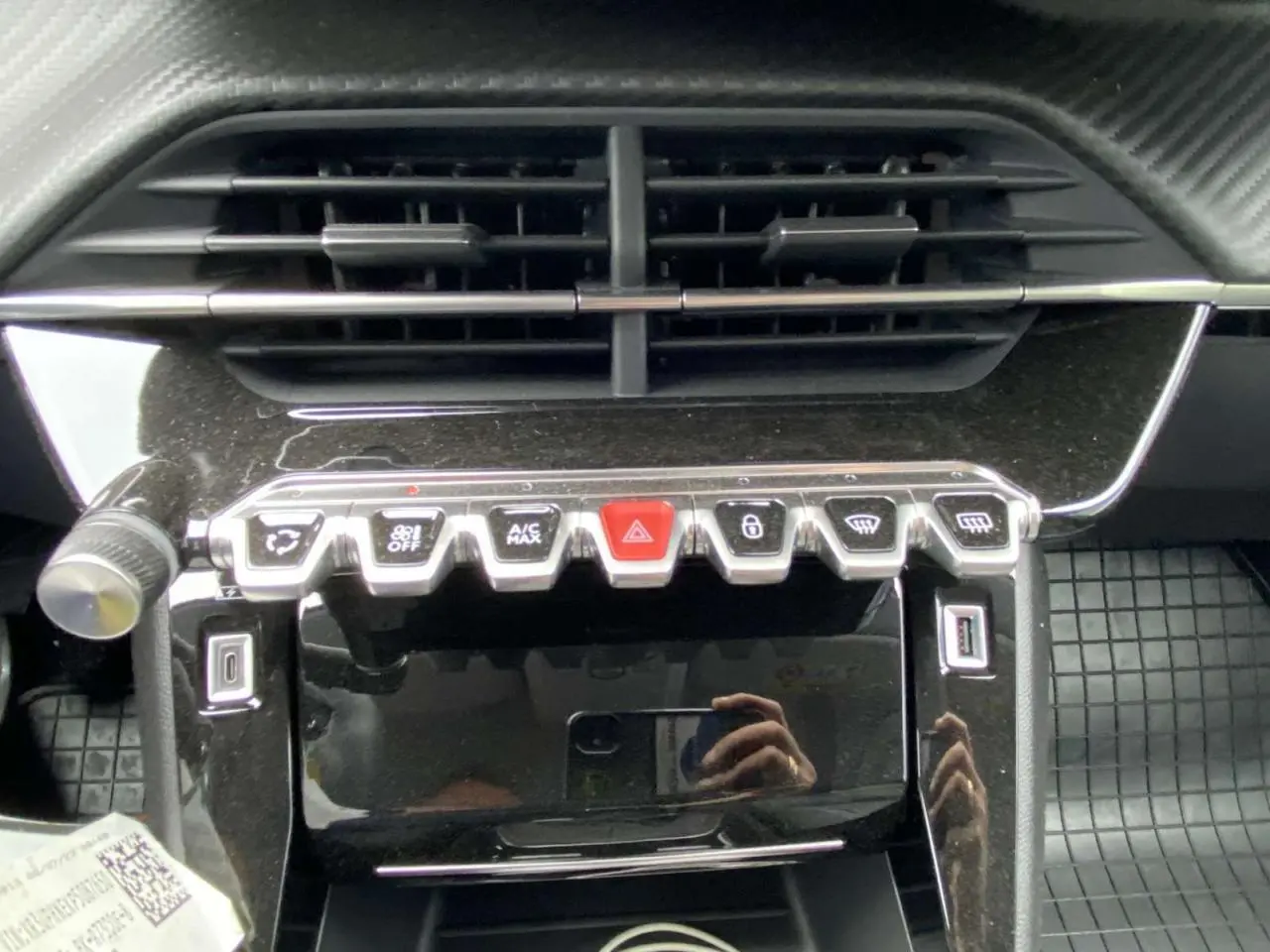 Vue rapprochée de la console centrale noire brillante de la Peugeot 208 avec boutons de commande et prises USB visibles.