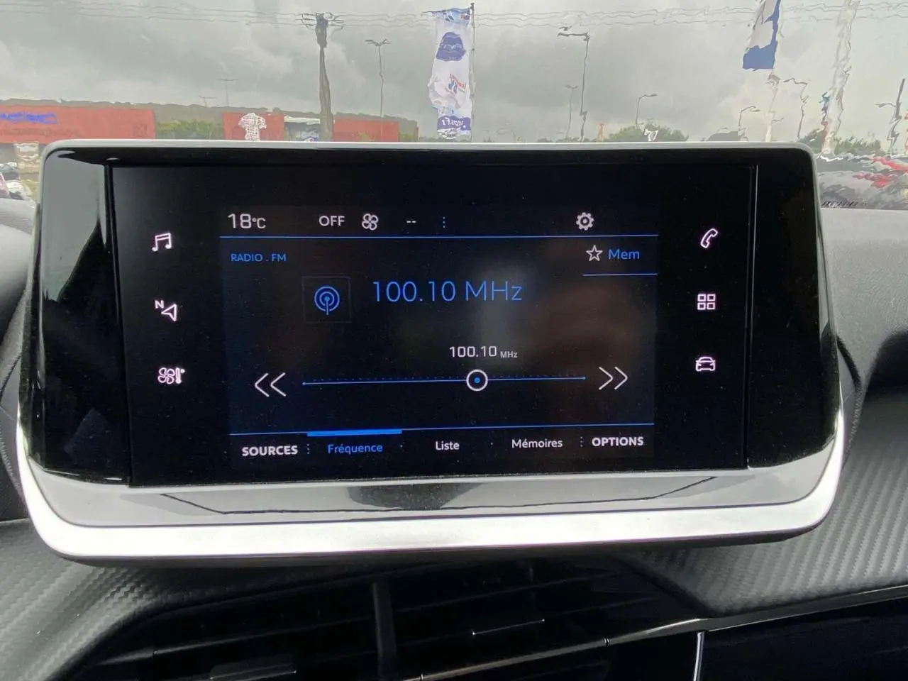 Écran tactile central de la Peugeot 208 2023 affichant la radio FM sur fond noir et détails lumineux blancs et bleus.