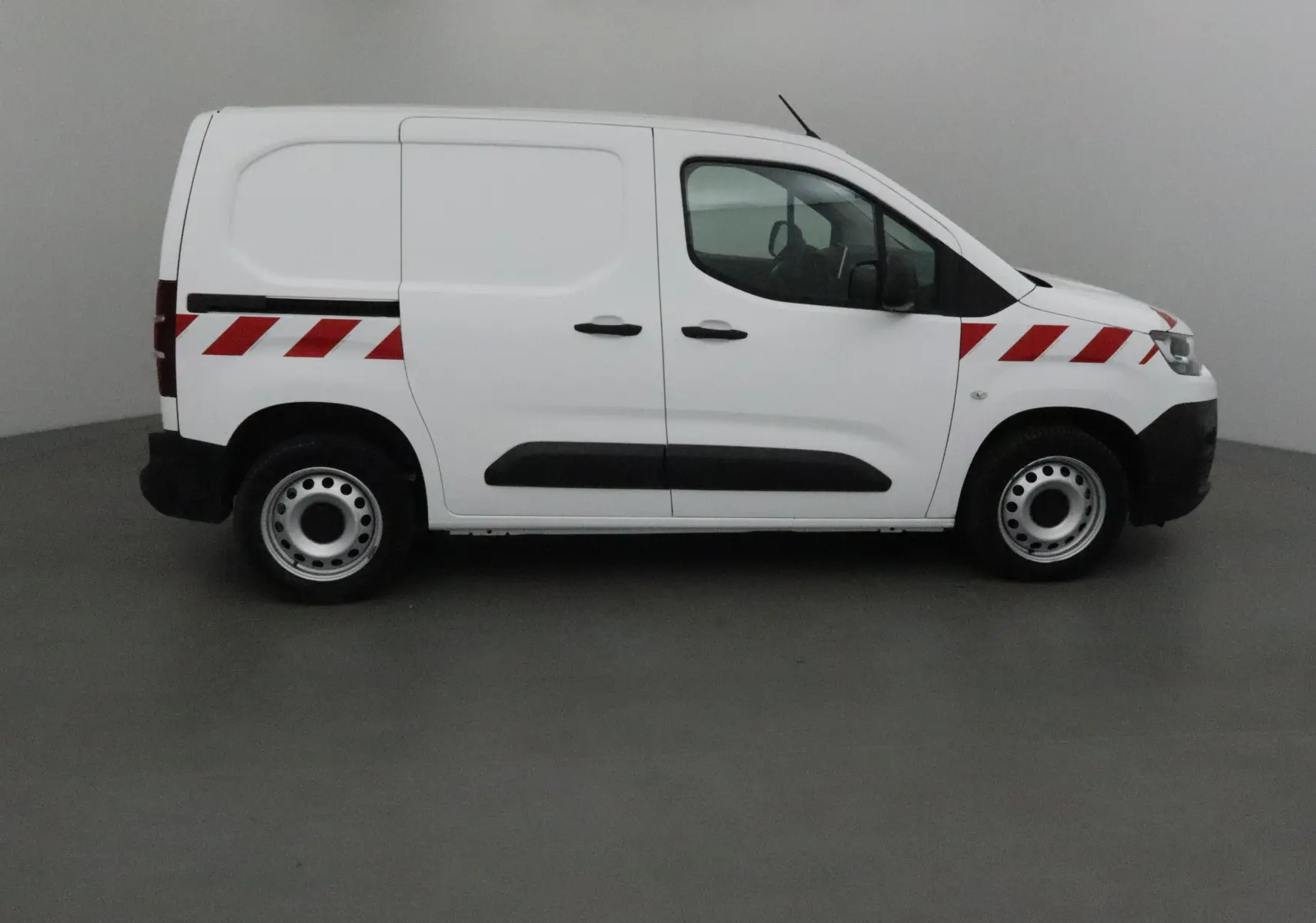 Profil côté gauche d'un utilitaire blanc Citroën Berlingo 2019 avec bandes rouges diagonales sur la carrosserie.