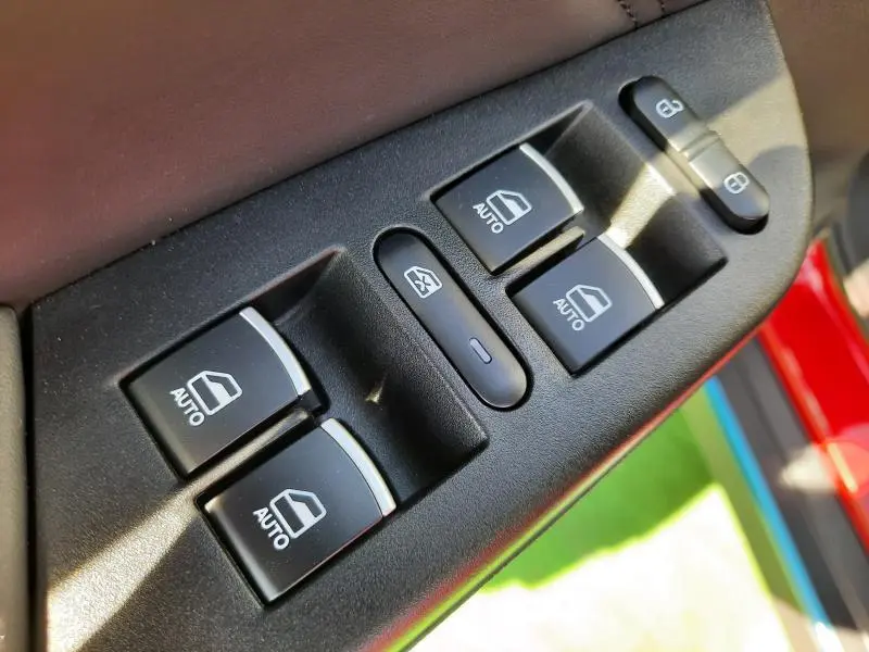 Gros plan sur les commandes de lève-vitres et verrouillage côté conducteur d'une SERES 3 rouge carmin 2023.