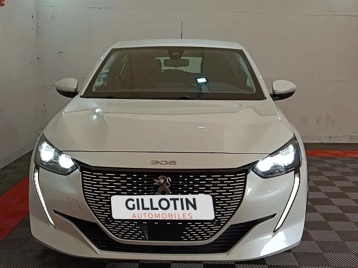 Vue frontale d'une Peugeot 208 électrique Active Business blanche avec phares LED allumés et calandre distinctive.