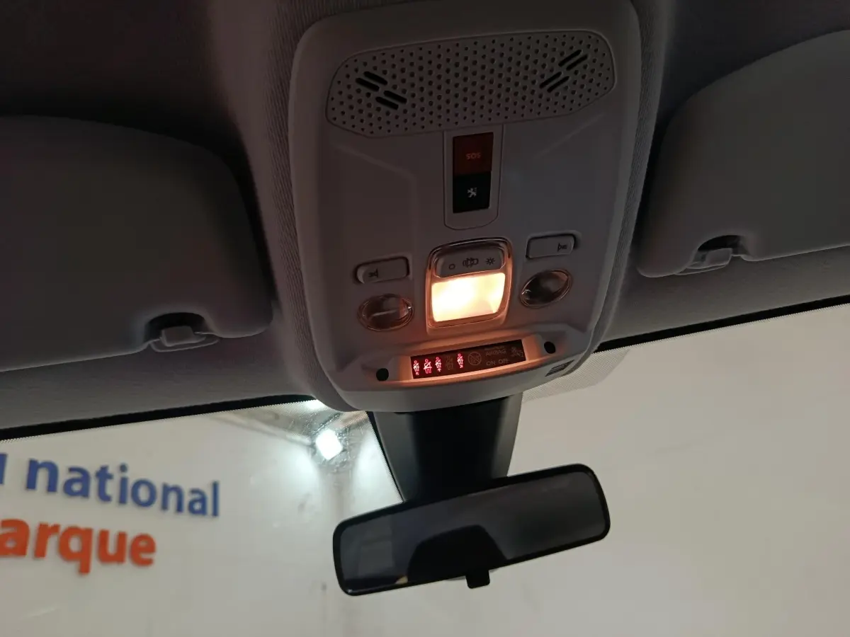 Vue intérieure du plafonnier allumé avec commandes et rétroviseur central d'une Peugeot 208 blanche électrique.
