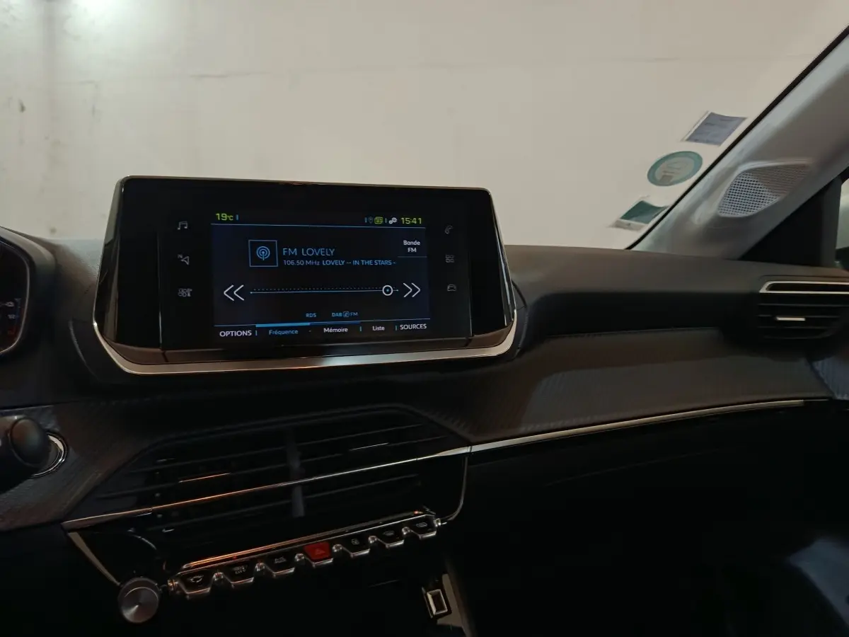 Vue intérieure du tableau de bord noir du Peugeot 208 électrique avec écran tactile central allumé.