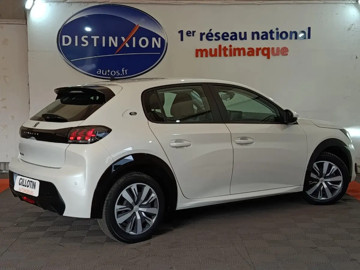 Vue latérale droite d'une Peugeot 208 électrique Active Business blanche, avec jantes spécifiques et feux arrière LED distinctifs.