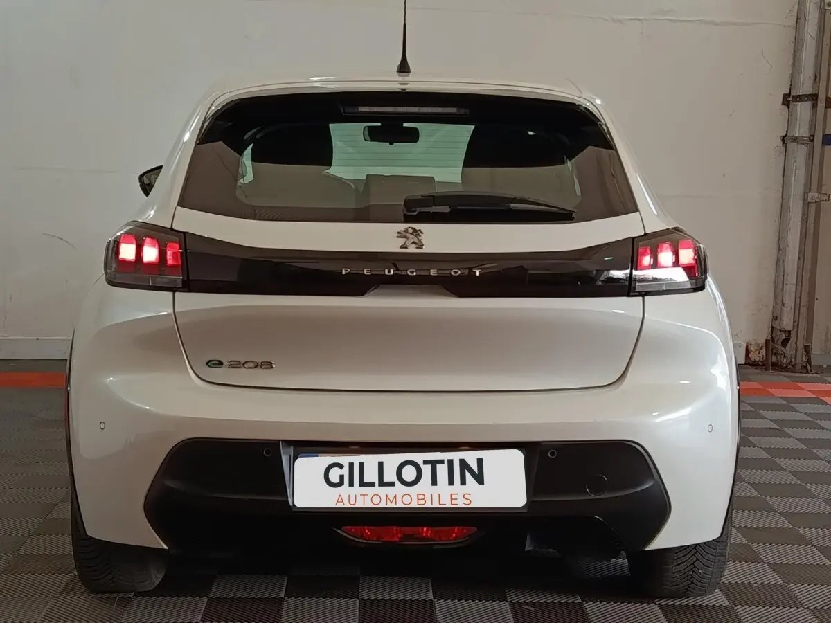 Vue arrière d'une Peugeot 208 électrique blanche avec feux arrière LED allumés dans un garage.