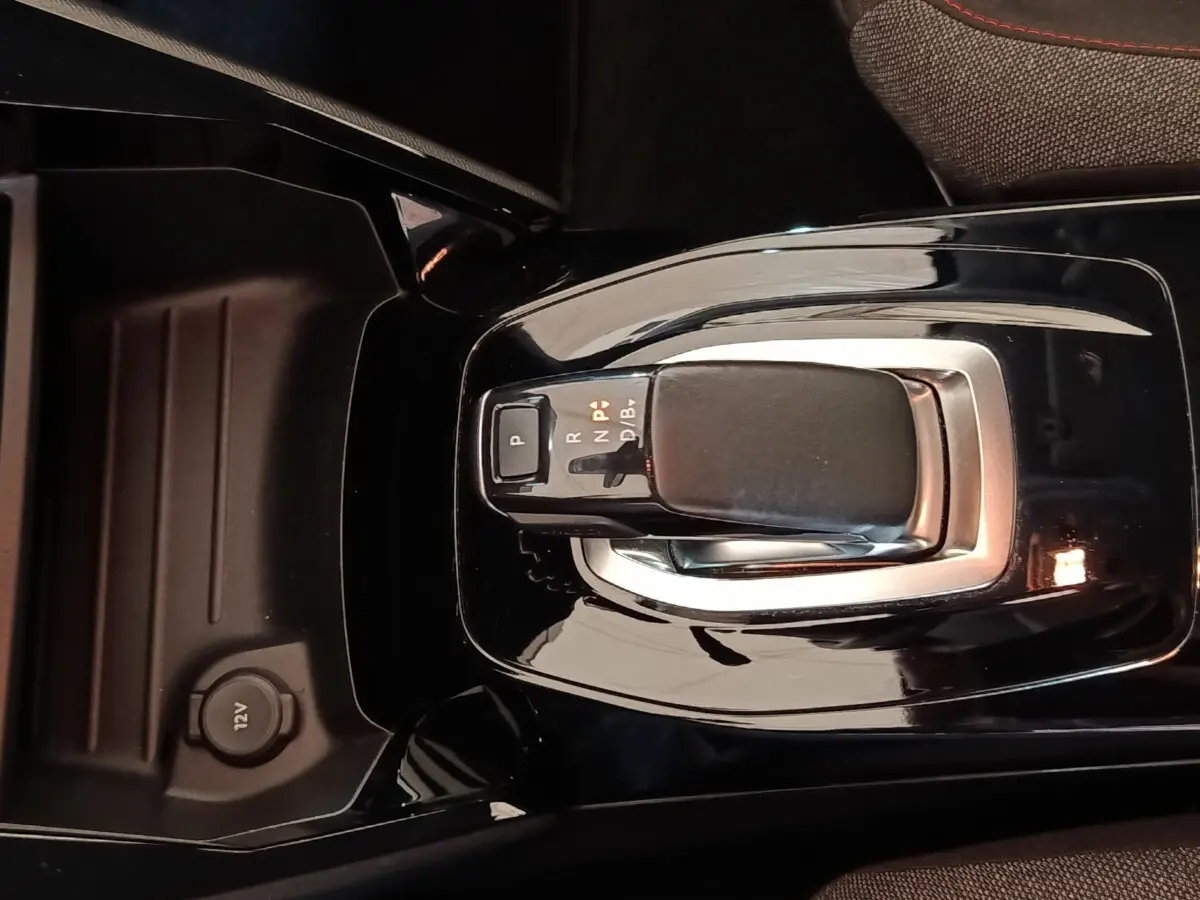 Gros plan sur la commande de boîte automatique noire au centre de la console d’une Peugeot 208 électrique blanche.