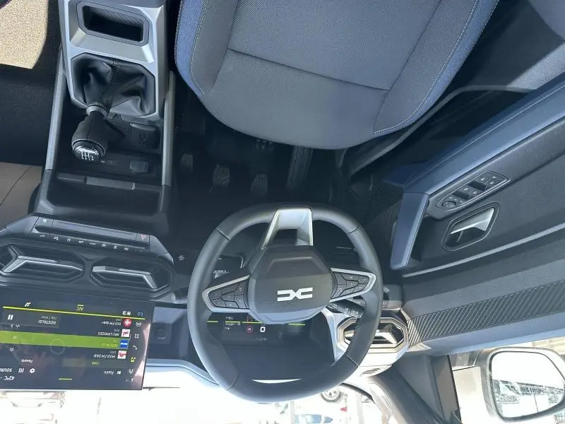 Vue intérieure du poste de conduite du Dacia Duster blanc 2025, volant multifonction et levier de vitesse manuel visibles.