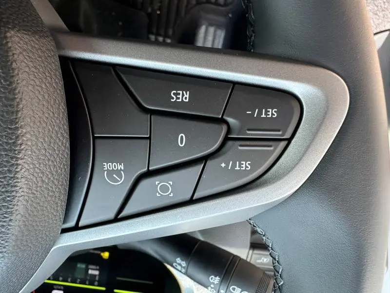 Gros plan sur les commandes de régulateur de vitesse au volant du Dacia Duster blanc 2025, côté gauche.