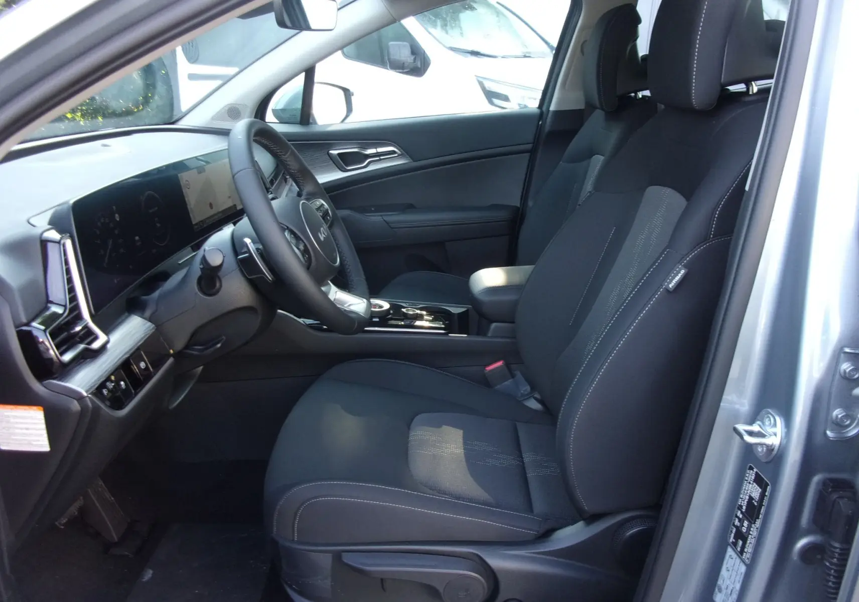 Vue intérieure côté conducteur du Kia Sportage gris perle 2025, mettant en valeur les sièges noirs et le tableau de bord moderne avec écran tactile.