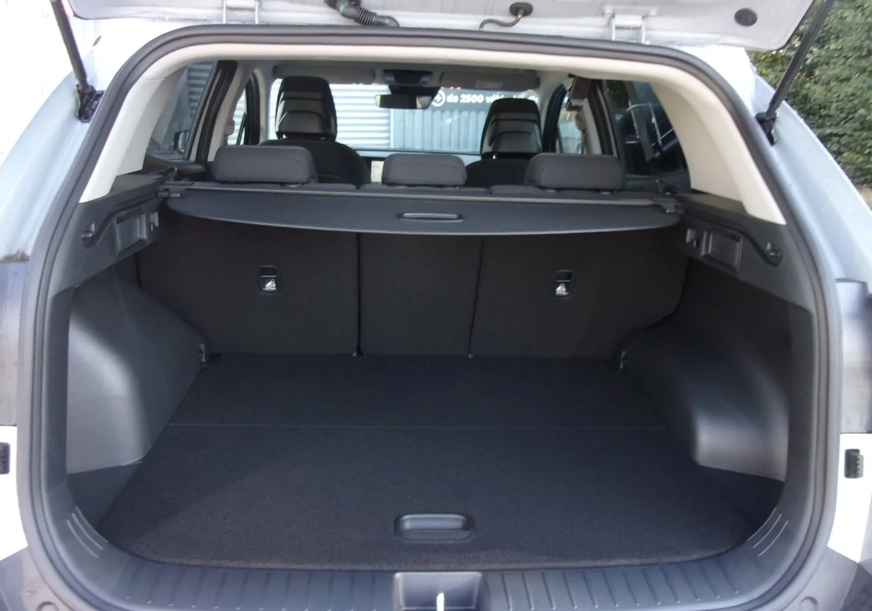 Coffre ouvert du Kia Sportage gris perle 2025, vue arrière montrant l'espace de chargement et les sièges arrière.