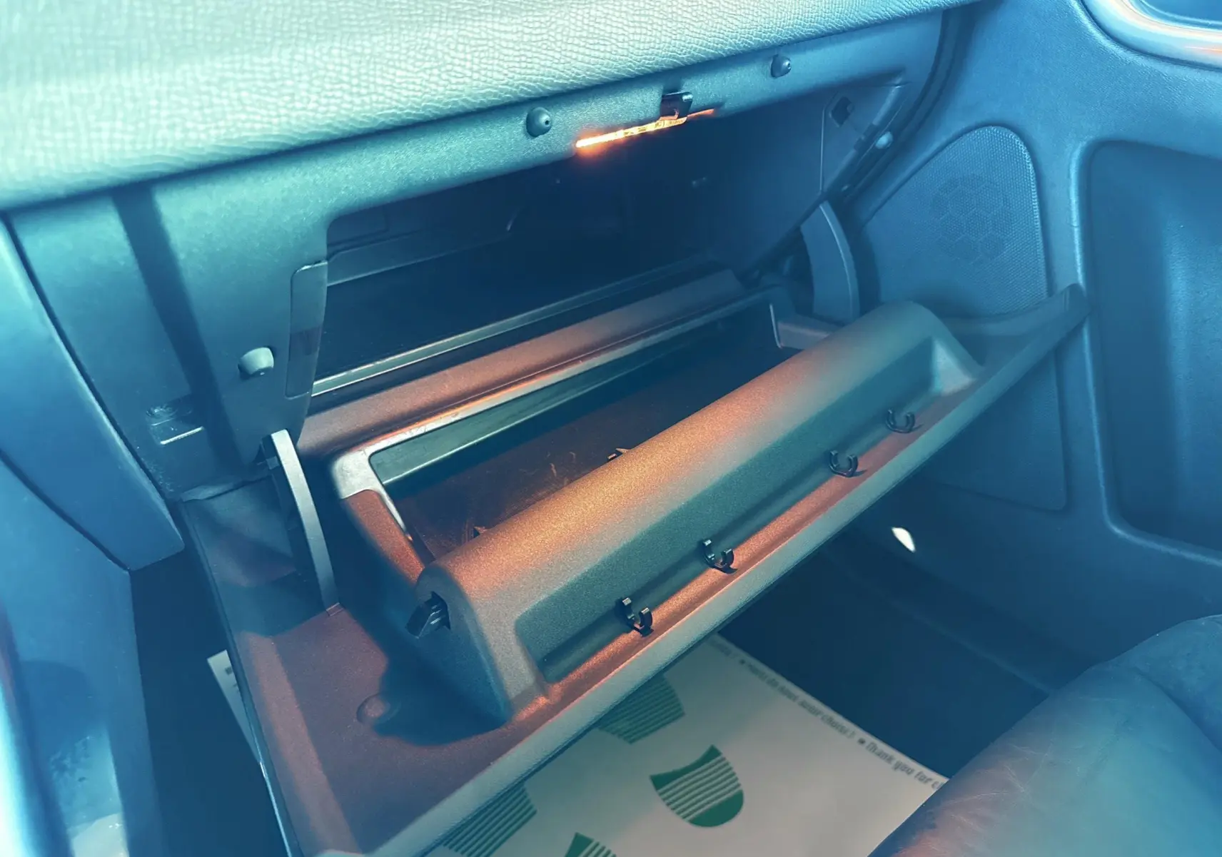 Gros plan sur la boîte à gants ouverte côté passager du Volvo XC60 gris, intérieur noir avec éclairage intérieur allumé.