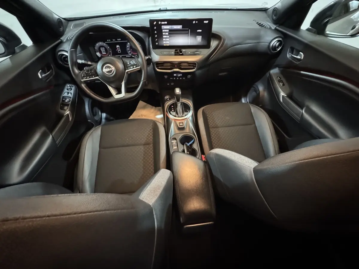 Vue intérieure avant du Nissan Juke gris clair 2025, avec tableau de bord numérique et écran tactile central.