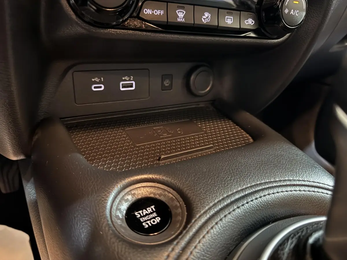 Gros plan intérieur sur la console centrale noire du Nissan Juke gris clair, montrant le bouton démarrage et ports USB.