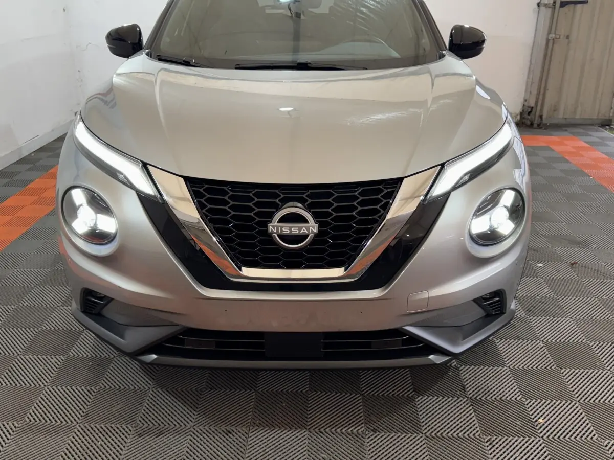 Vue frontale d'un Nissan Juke gris clair avec phares LED allumés dans un garage.