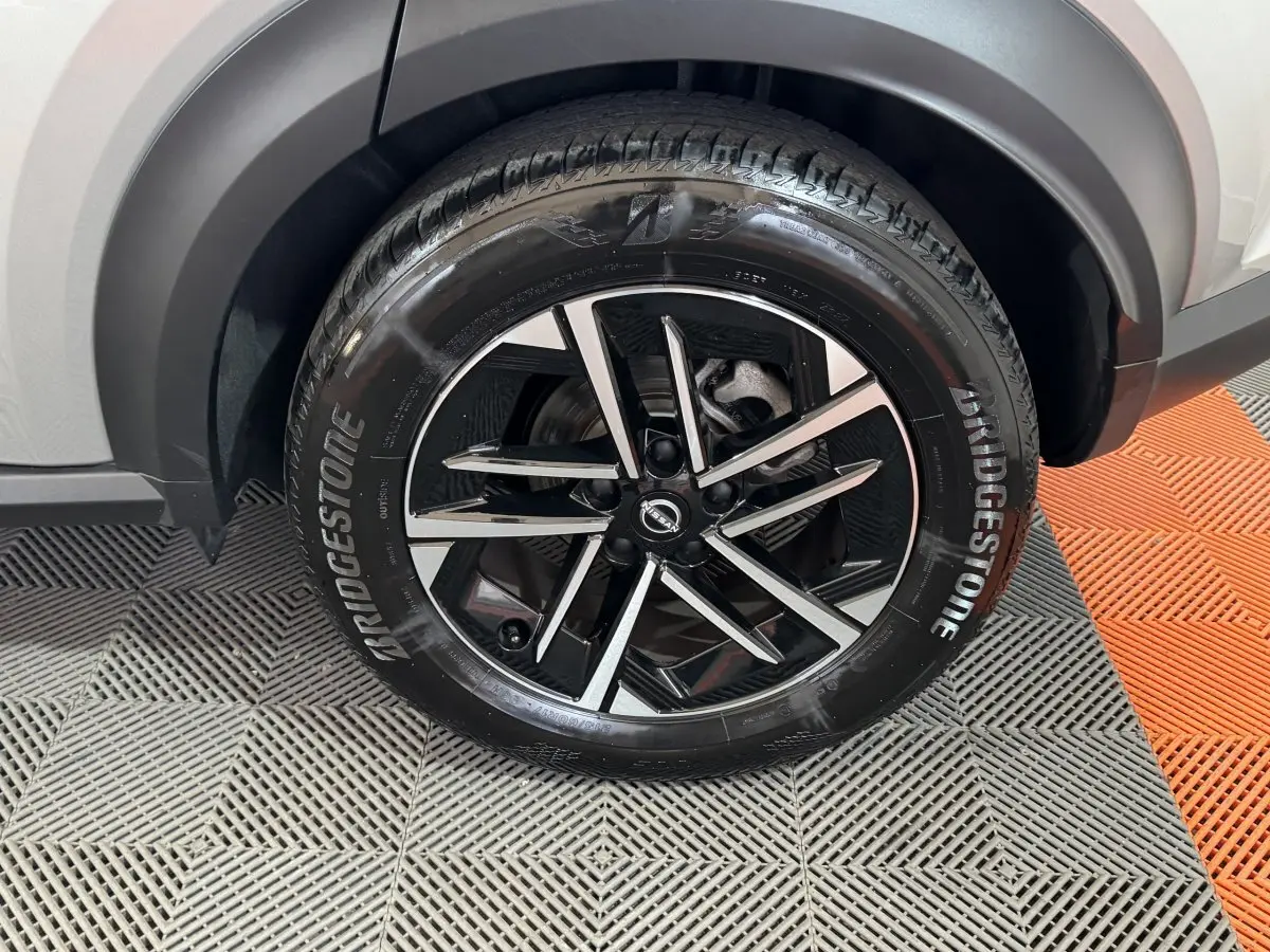 Gros plan sur la roue avant droite du Nissan Juke gris clair, mettant en valeur la jante noire et argentée au design moderne.