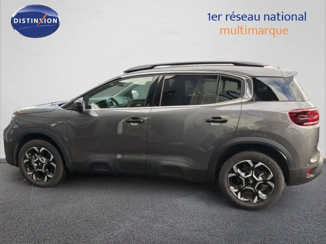 Citroën C5 Aircross Hybrid gris platinium en 3/4 avant droit avec jantes bicolores et barres de toit noires.