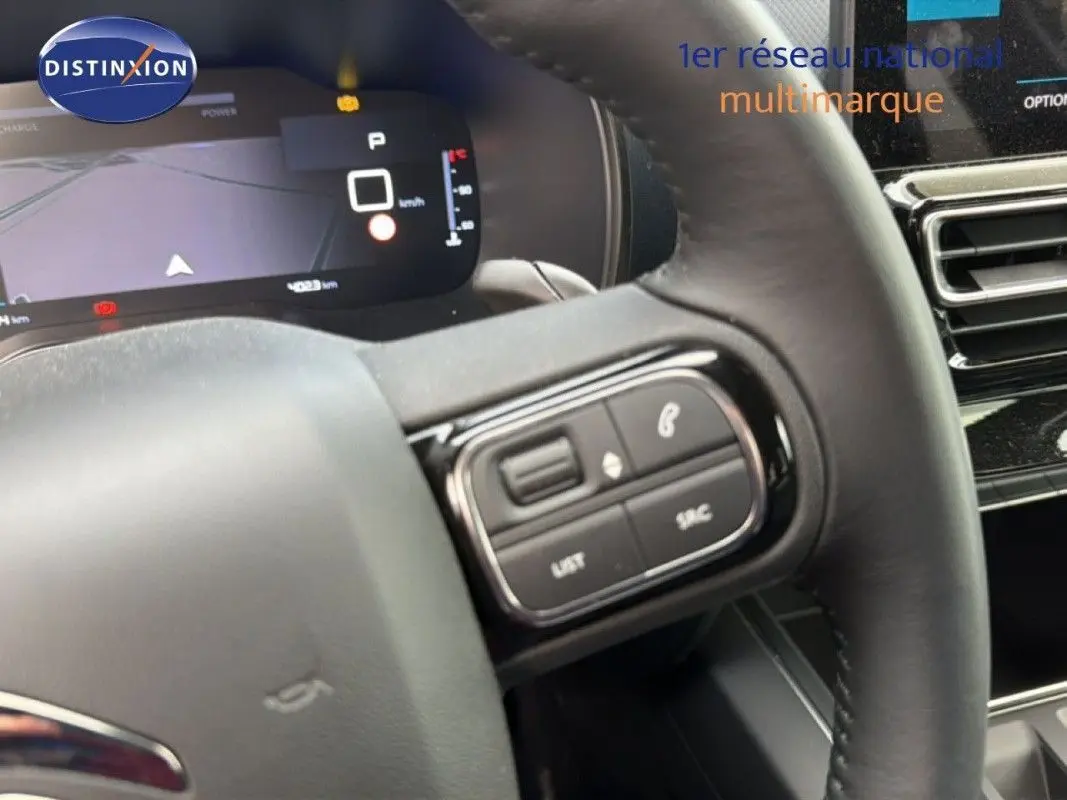 Gros plan sur le volant et le tableau de bord numérique du Citroën C5 Aircross Hybrid gris platinium, avec commandes au volant visibles.